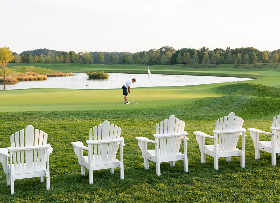 Golfer putting on green with Adirondack chairs in foreground